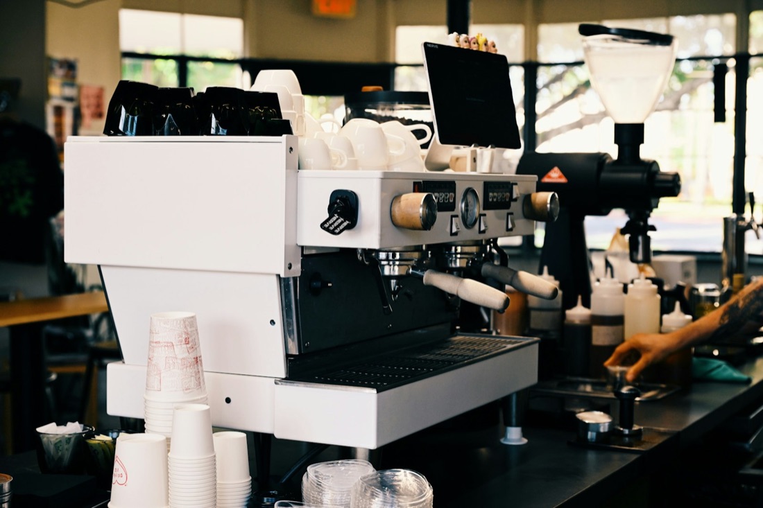 A barista working an espresso machine at a café counter in morning light
